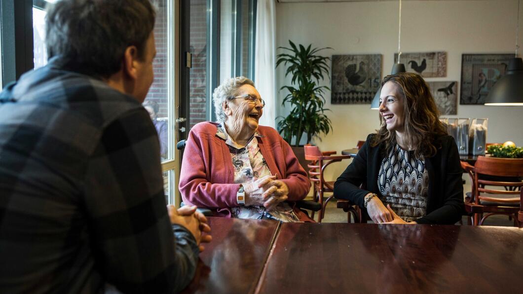 Ouderen aan tafel in gesprek met een jongere (verzorger)